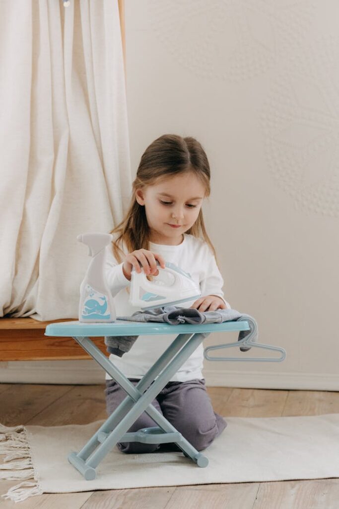 Cute little girl pretending to iron with a toy set indoors, showcasing imaginative play.