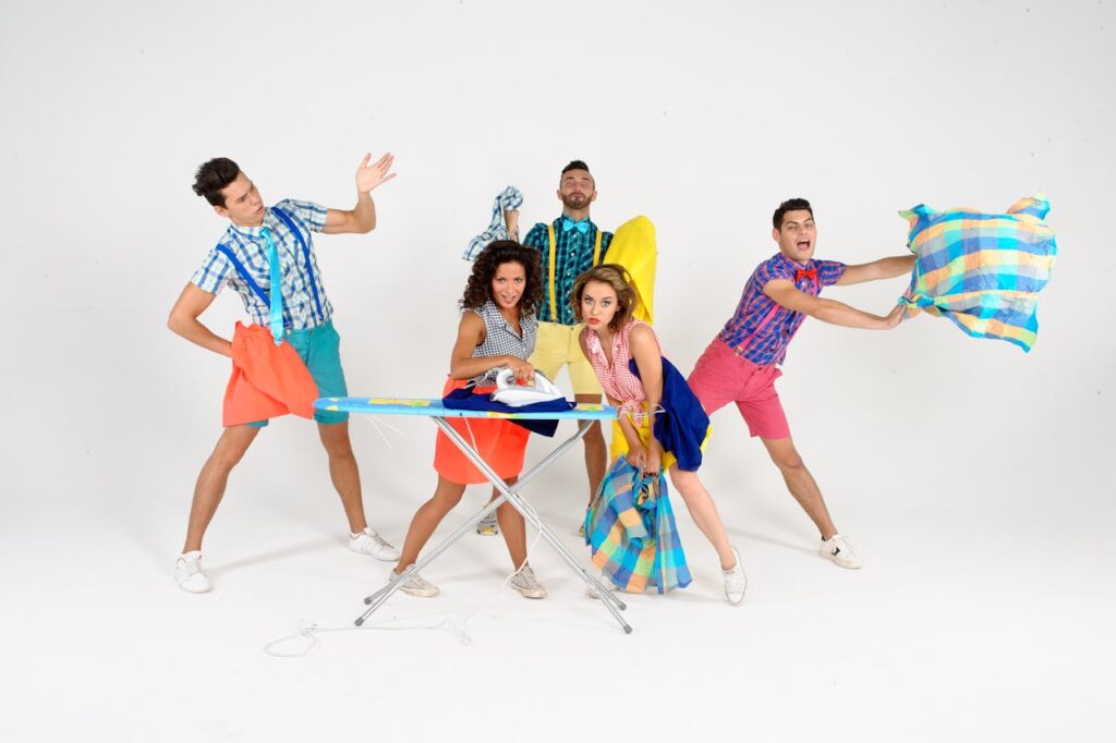 Group of diverse adults humorously posing around an ironing board with playful expressions.