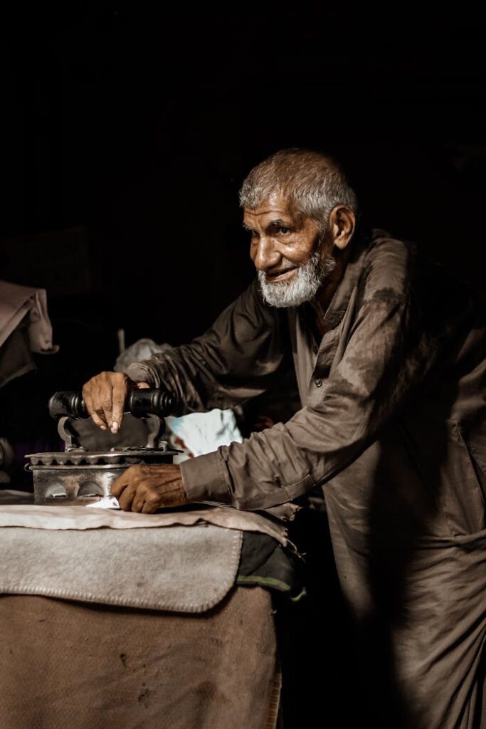An elderly man irons clothes in a traditional workshop in Multan, Pakistan, showcasing craftsmanship.